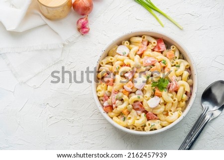 Homemade macaroni salad with elbow pasta, onion, carrot, tomato, green peas and mayonnaise dressing in a white bowl on a white wooden table.Top view Royalty-Free Stock Photo #2162457939
