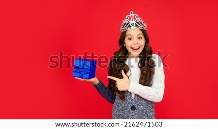 amazed child in queen crown. princess in tiara pointing finger on box.