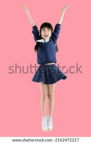 Happy smiling face of little Asian girl child dancing on isolated pink background. Joyful portrait of Asian elementary school student.