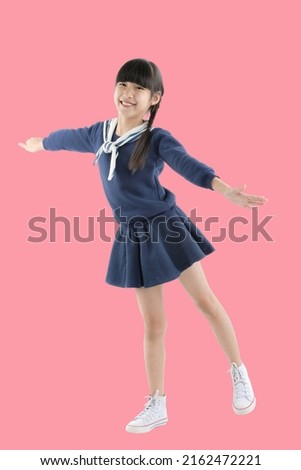 Happy smiling face of little Asian girl child dancing on isolated pink background. Joyful portrait of Asian elementary school student.