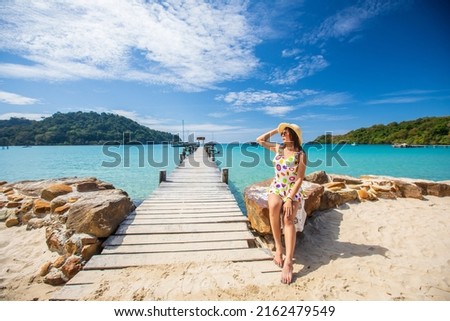 Young Asian lady tourist sitting on the sand stone  in to the sea on her holiday.