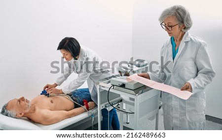 Cardiogram test. Elderly male patient receives heart rate monitored using electrocardiogram equipment with two doctors cardiologist Royalty-Free Stock Photo #2162489663