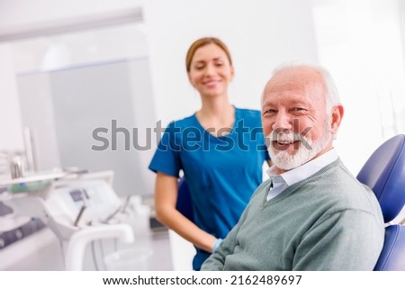 Portrait of satisfied senior male patient sitting at dental chair at dentist office smiling with doctor in the background Royalty-Free Stock Photo #2162489697