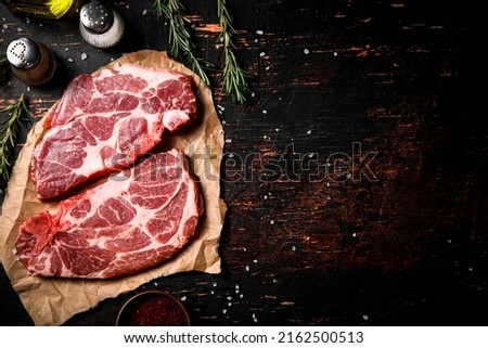 Raw pork steak on paper with rosemary. Against a dark background. High quality photo