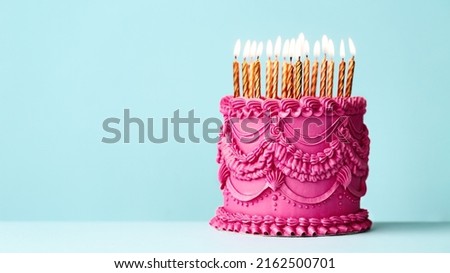 Fancy pink birthday cake with vintage style buttercream frills and ruffles and gold birthday candles against a blue background