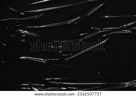 Transparent plastic wrap on black background. Crumpled wrinkled plastic cellophane. Reflecting light and shadow on creases and folds in plastic surface. Texture overlay effect template Royalty-Free Stock Photo #2162507737