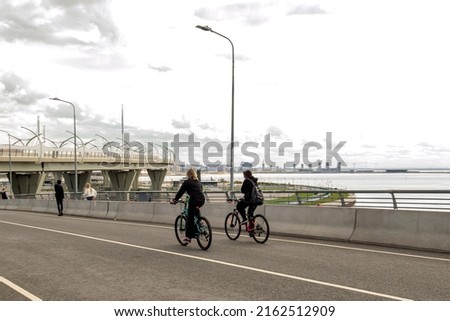 Two girls ride bicycles on a bridge over the bay