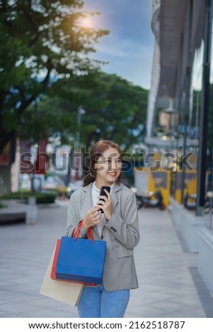 Happy Asian woman standing in front of a shopping mall at a shopping center. . Asian woman holding shopping bags, woman concept shopping stand and vertically holding multicolored paper bags.