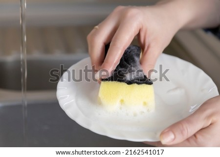 Washing a white plate with a sponge with dishwashing liquid with foam.