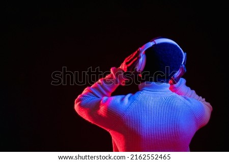 Music chill. Futuristic gadget. Night entertainment. Unrecognizable man in headphones listening to song in vivid red neon light on dark empty space background.