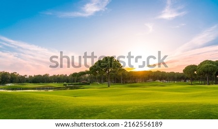 Panorama of golf course at sunset with beautiful sky. Scenic panoramic view of golf fairway. Golf field with pines Royalty-Free Stock Photo #2162556189