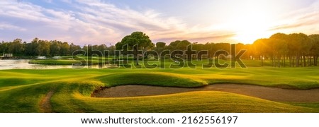 Golf course at sunset with beautiful sky and sand trap. Scenic panoramic view of golf fairway with bunker. Golf field with pines Royalty-Free Stock Photo #2162556197