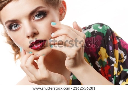 A young and beautiful girl with dark makeup smears dark lipstick on her lips.