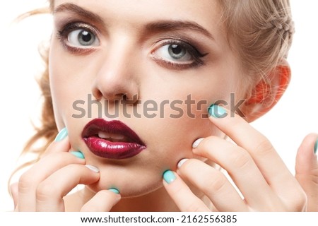 A young and beautiful girl with dark makeup smears dark lipstick on her lips.