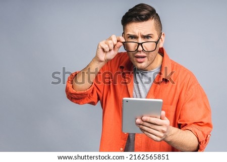 Shocked amazed young ukrainian man in casual standing and using tablet isolated over grey white background.