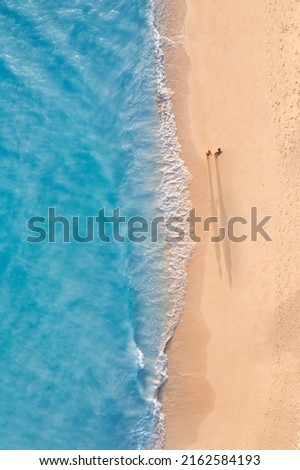 Aerial view of couple walking on beach with sunlight close to turquoise sea waves. Top view of summer beach landscape, romantic inspirational couple vacation, romance holiday. Freedom travel template
