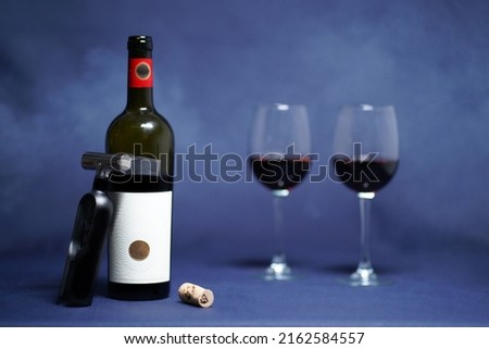 Opened dry, red wine and an exclusive corkscrew with a cork including two wine glasses. (Whole picture with smoke and grey background)                               
