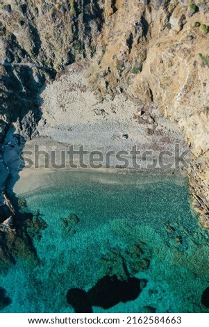 Aerial top down drone photo of a hidden beach with turquoise waters in mykonos during summer