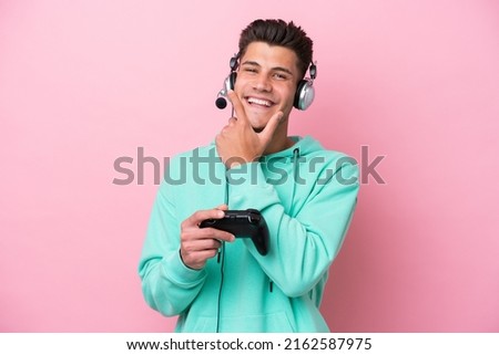 Young handsome caucasian man playing with a video game controller isolated on pink background happy and smiling