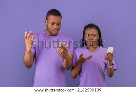 Strange Message, Bad News, Internet Connection Problem. Confused sad millennial African American couple looking at their phones and shrugging shoulders, standing isolated on purple violet background Royalty-Free Stock Photo #2162590139