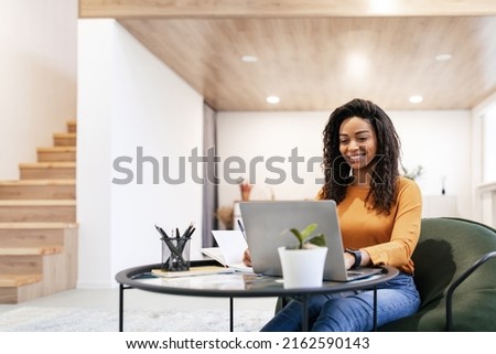 Portrait of smiling woman sitting at desk, using laptop and writing in notebook, taking notes, watching tutorial, lecture or webinar, studying online at home looking at screen, free copy space Royalty-Free Stock Photo #2162590143