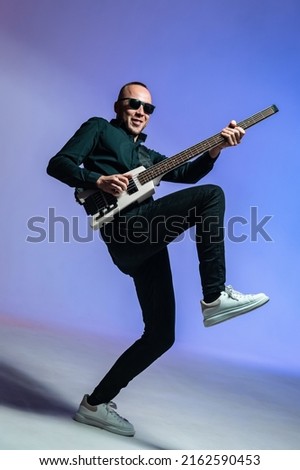 Epathetic rock musician, bass guitarist in the studio with a bass in his hands. Colorful background