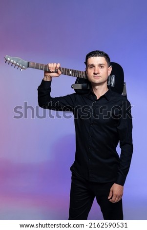 Cheerful guitarist in black clothes with a black electric guitar in his hands. Colorful background