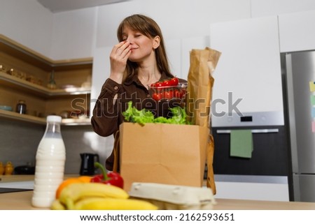 Woman at kitchen unpacks a paper bag with groceries from a supermarket and sniffs fresh tomatoes