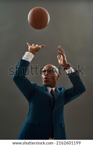 Concentrated black entrepreneur or ceo manager throwing basketball ball. Bald adult man wearing formal wear. Modern successful male lifestyle. Concept of business goal. Grey background. Studio shoot