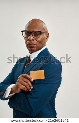 Serious black entrepreneur showing golden business card. Bald adult man wearing formal wear and glasses looking at camera. Modern successful male lifestyle. Isolated on white background in studio. 