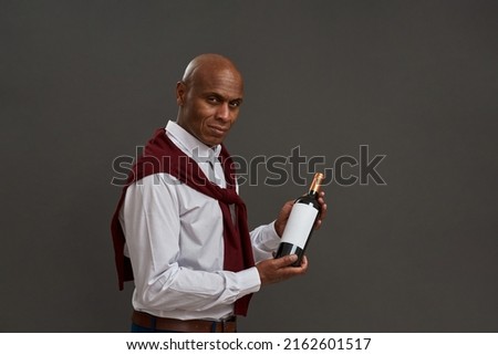 Side view of black winemaker or sommelier holding wine bottle. Adult successful male entrepreneur or businessman. Viticulture and winemaking. Isolated on grey background. Studio shoot. Copy space