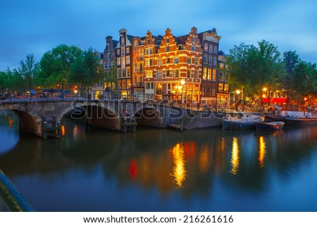 Night city view of Amsterdam canal, bridge and typical houses, boats and bicycles, Holland, Netherlands. 