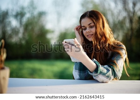 Young girl blogger freelancer holding her phone looking at it and working outdoors in a green park pensively looking at the screen online Royalty-Free Stock Photo #2162643415