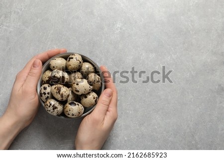 Woman holding bowl of quail eggs at light grey table, top view. Space for text