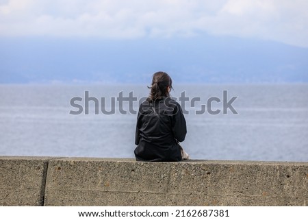 A woman sitting on a breakwater and staring at the sea Royalty-Free Stock Photo #2162687381