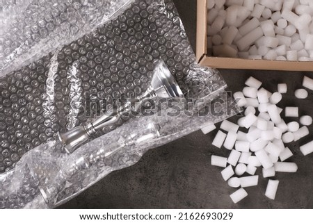 Elegant silver candlesticks, bubble wrap and cardboard box with foam peanuts on dark grey table, flat lay