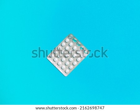 Colorful pills of white color in blister on blue plain background