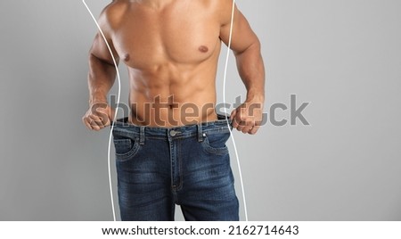 Closeup view of man with muscular body in oversized jeans on grey background, space for text. Weight loss Royalty-Free Stock Photo #2162714643