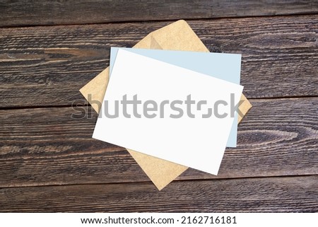 Mockup of an invitation and an envelope made of craft paper against a background of rough dark boards. Mockup to show invitation or greeting card design.