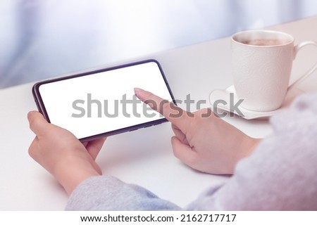 mockup cellphone horizontal position. Cropped shot view of female hands holding cellphone with blank screen for text in cafe. woman typing text on phone in cafe at white table Royalty-Free Stock Photo #2162717717