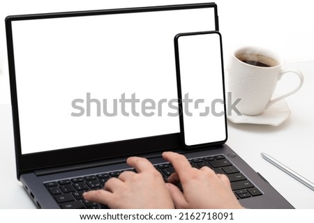 Mockup device. cell phone and laptop use at same time. female hands typing on laptop keyboard with blank white screen. businesswoman using smartphone and notebook with blank screen at workplace desk.