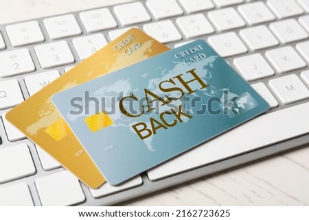 Cashback credit cards and keyboard on white wooden table, closeup