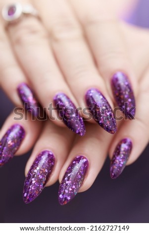 Beautiful female hands with long nails and purple plum manicure holds a bottle of nail polish