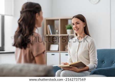 psychology, mental health and people concept - smiling psychologist with notebook and woman patient at psychotherapy session Royalty-Free Stock Photo #2162737569