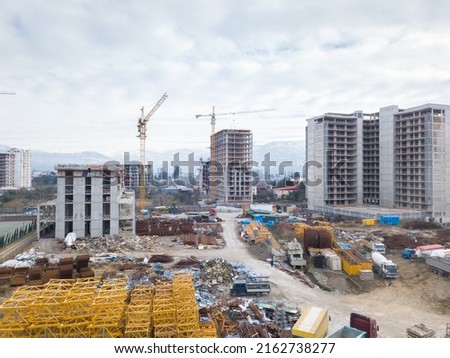 Drone view of the construction site, multi-storey buildings under construction against the background of mountains. Construction machinery, excavators, tractor crane