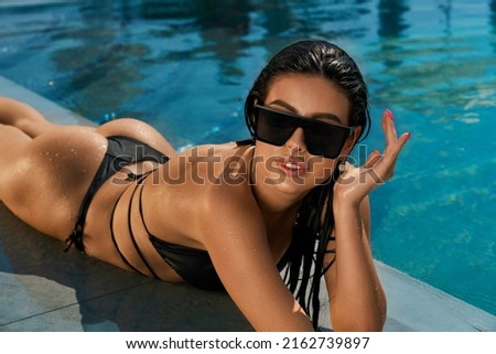 Side view of brunette girl with long wet hair swimming in pool. Beautiful slim female lying on abdomen, sunbathing, relaxing, looking aside. Concept of summertime and youth.