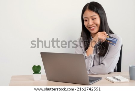 The Asian businesswoman's hand is holding a credit card and using a laptop for online shopping and internet payment in the office.