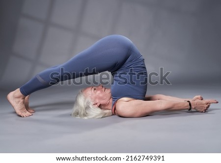 Senior woman with white hair training yoga, studio shot on gray background