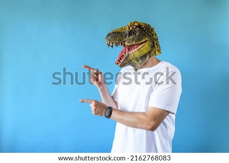 Funny laughing dinosaur head on human body on white t-shirt on blue background, pointing fingers to the left. Clip art, negative space.