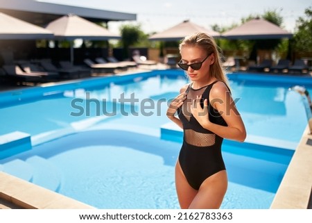 Fit woman in bikini sunbathing and chilling near swimming pool at a tropical spa. Attractive slim girl in swimwear and sunglasses posing at luxury resort. Hot female relaxing and enjoying the sun.